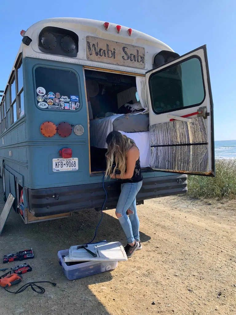 Victoria Neidhardt standing next to the back of a blue school bus converted into a home.