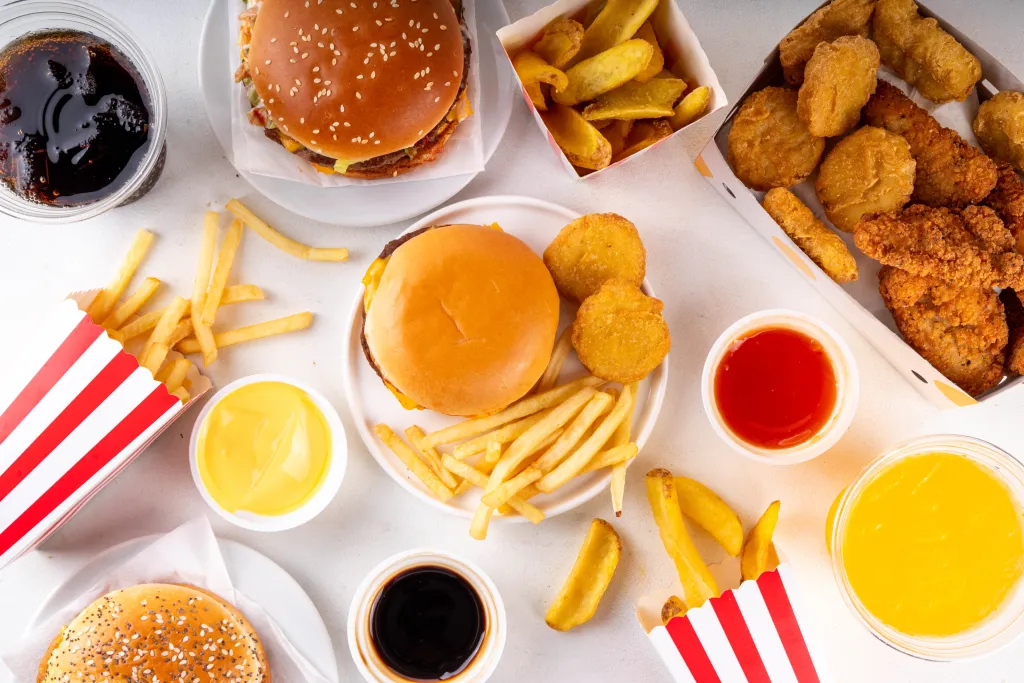 A top-down view of a spread of fast food items, including burgers, chicken nuggets and strips, french fries, potato wedges, and various drinks and dipping sauces.