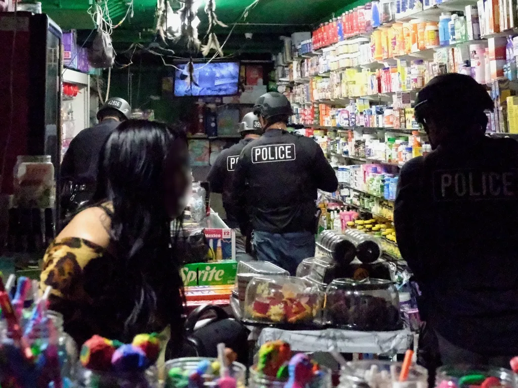Police officers in tactical gear inside a store with shelves of products.