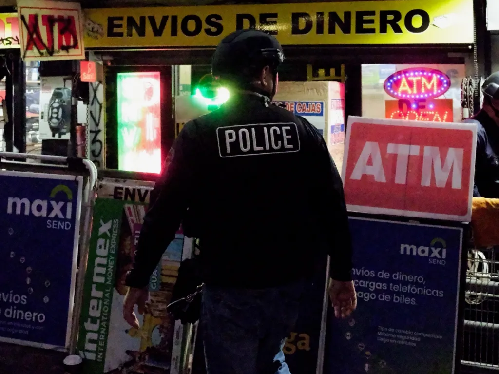 A police officer from behind walks past ATM signs and signs advertising money wiring services.