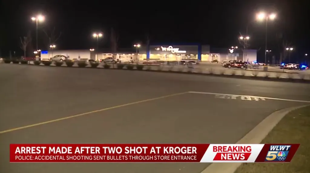 A Kroger store at night with flashing police lights in the parking lot and a news overlay reporting 