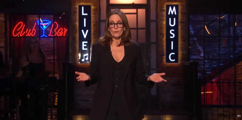 A woman in glasses and a black suit stands on a stage with