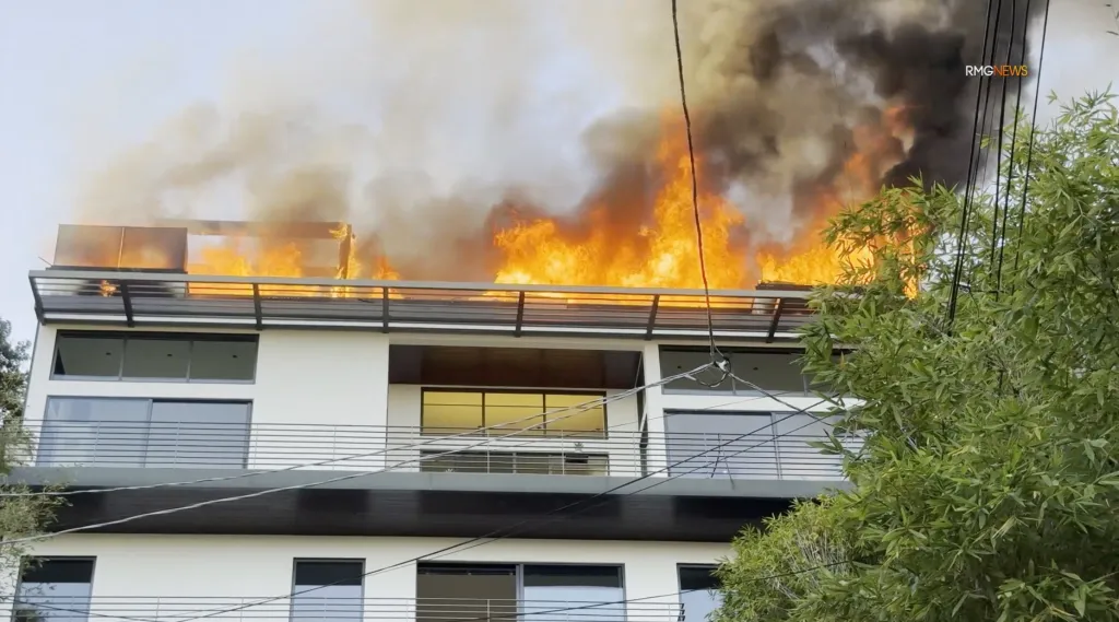 A multi-story mansion in West Hollywood engulfed in flames, with heavy fire showing through the roof.