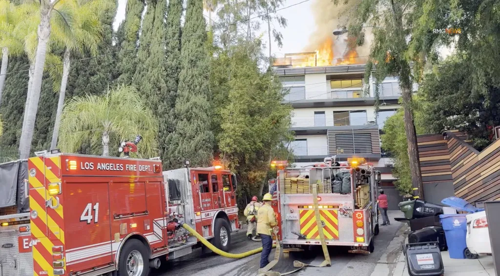 Los Angeles fire department responding to a multi-story mansion fire with heavy flames and smoke rising from the roof.