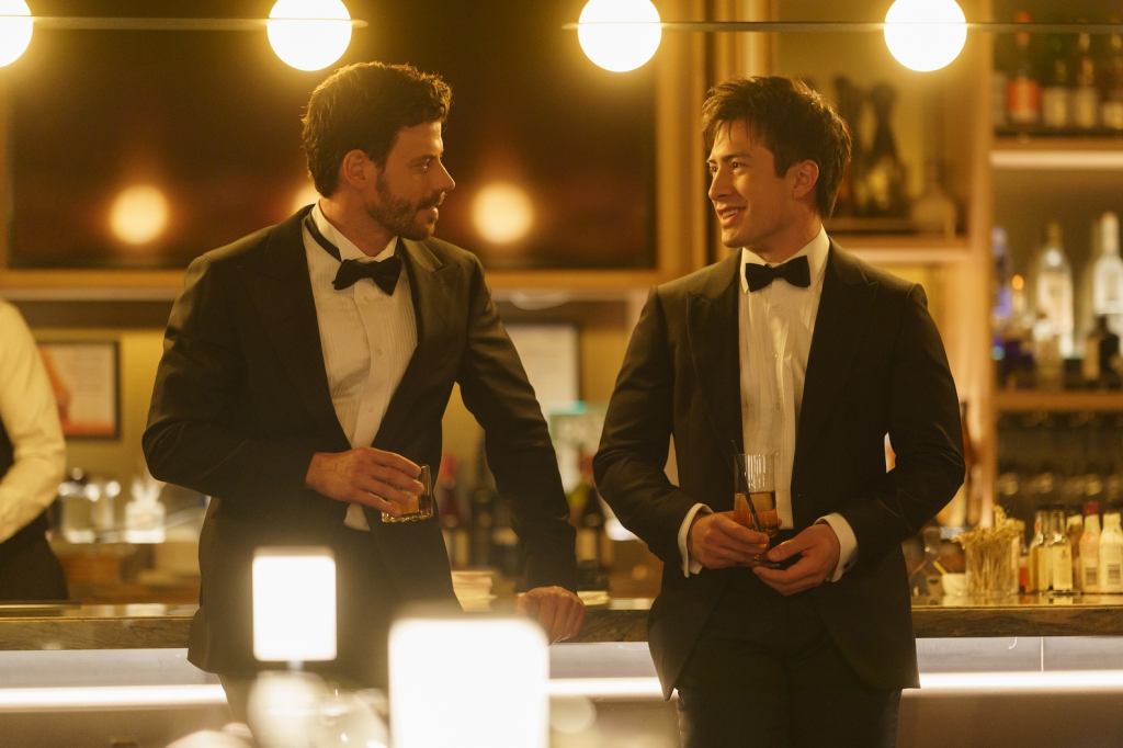 François Arnaud as Scott Hunter and Hudson Williams as Shane Hollander in tuxedos holding drinks at a bar.