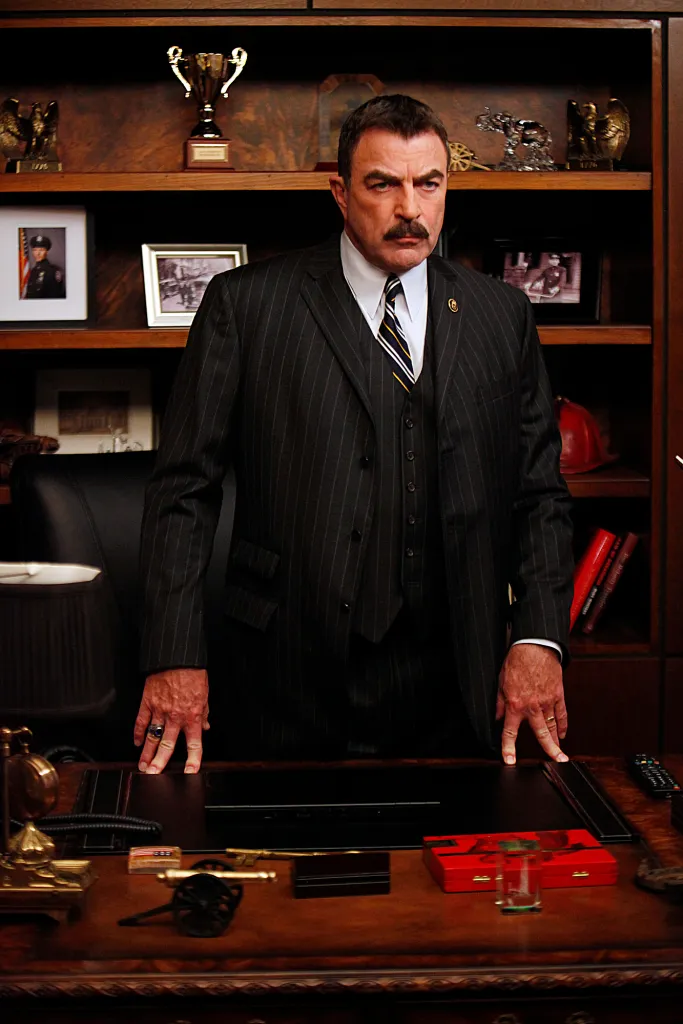 Frank Reagan (Tom Selleck) stands behind his desk.