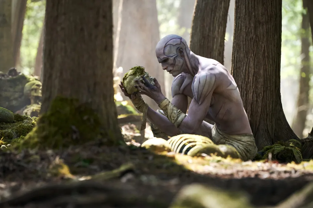 Jacob Elordi as The Creature holding a moss-covered skull in a forest.