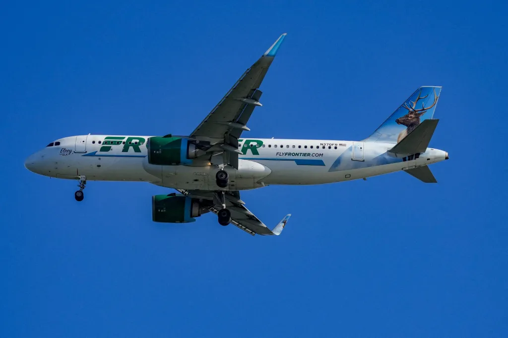A Frontier Airlines plane with a large elk painted on its tail, against a clear blue sky.