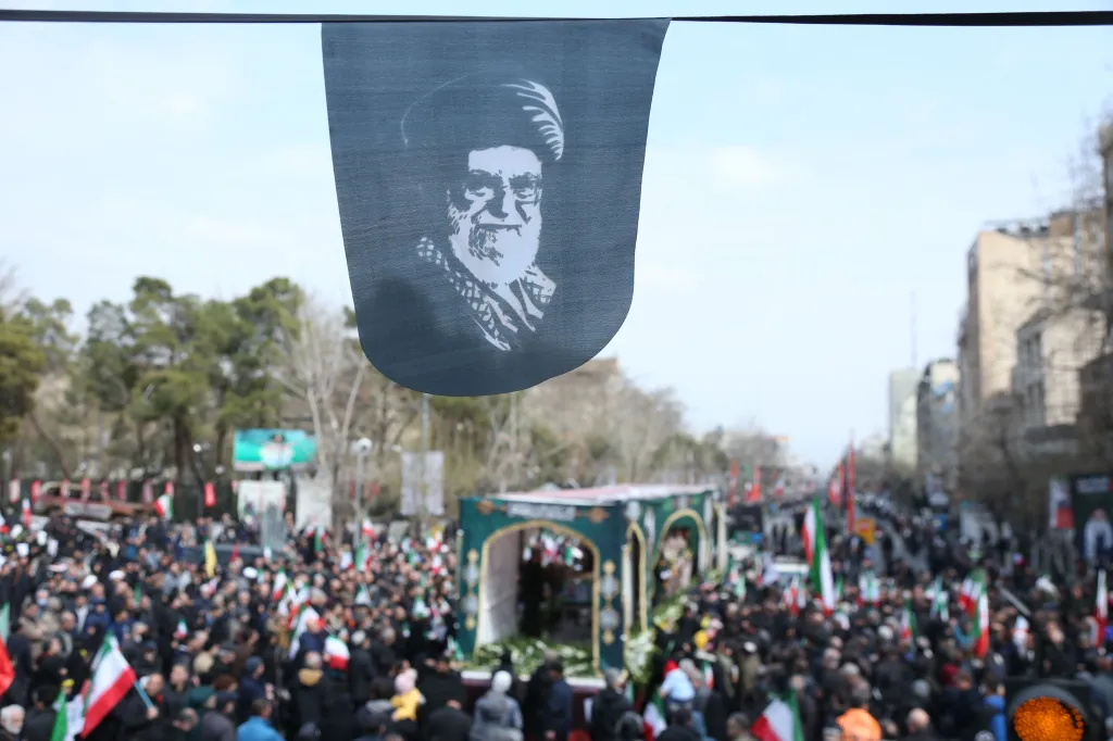 A banner with a portrait of Ayatollah Ali Khamenei hangs over a street filled with a large crowd attending the funeral procession for high-ranking military commanders in Tehran, Iran.