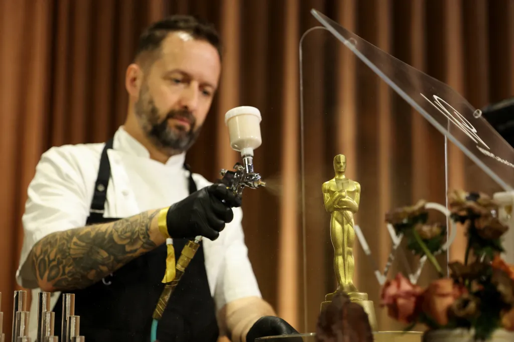 A pastry chef sprays an Oscar statue with edible gold paint.