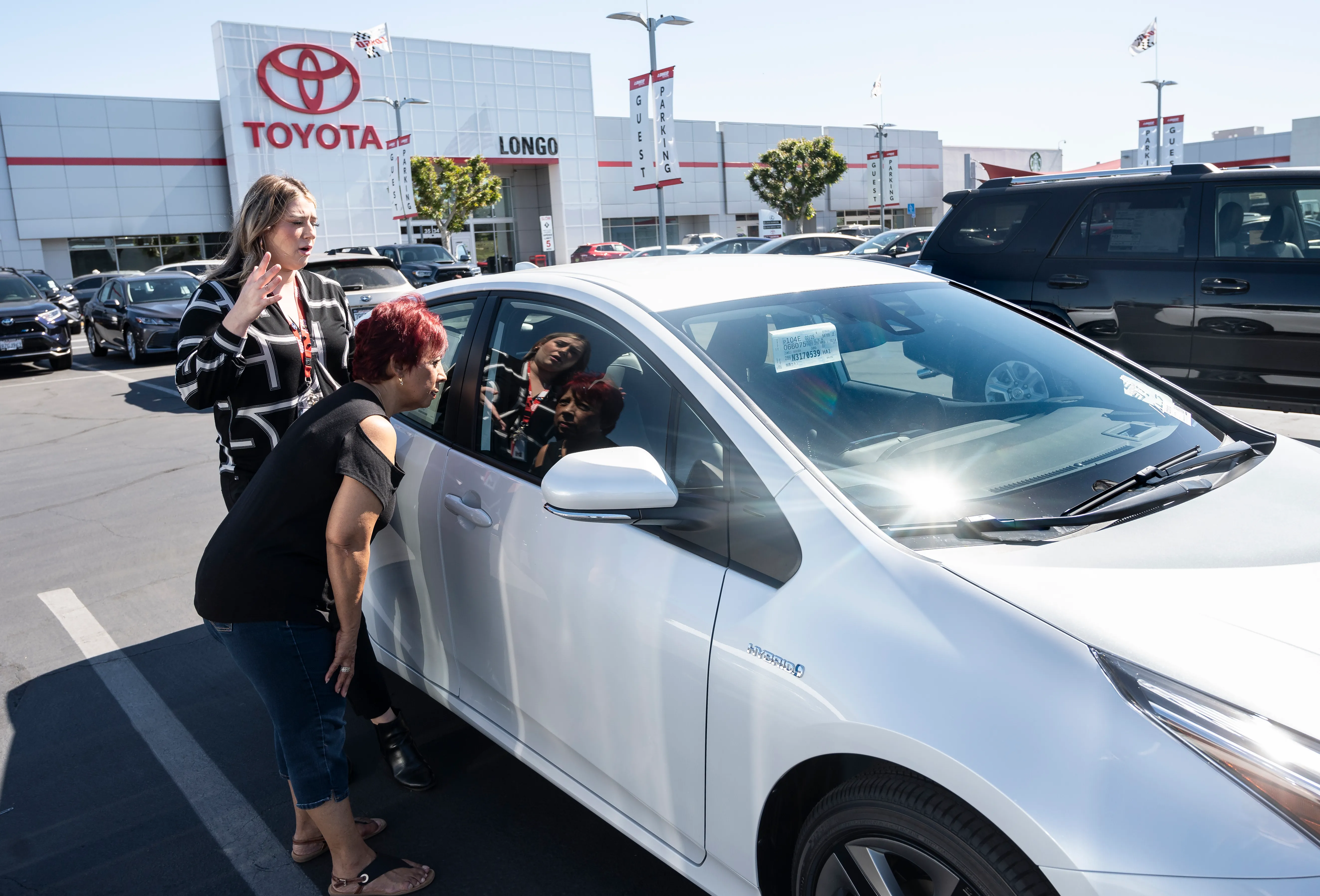 a customer is shown a 2022 white toyota prius car at a toyota dealership lot outdoors a customer is shown a 2022 white toyota prius car at a toyota dealership lot outdoors