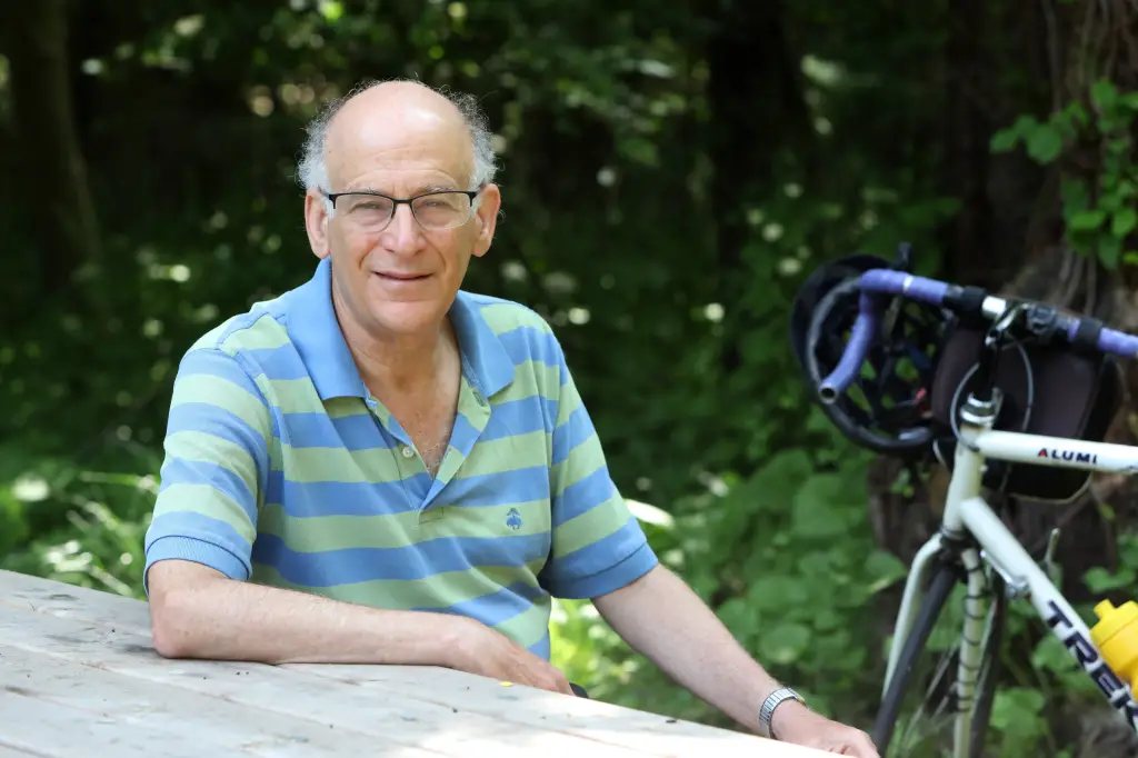 Greenburgh Town Supervisor Paul Feiner sitting at a wooden picnic table with a bicycle beside him.
