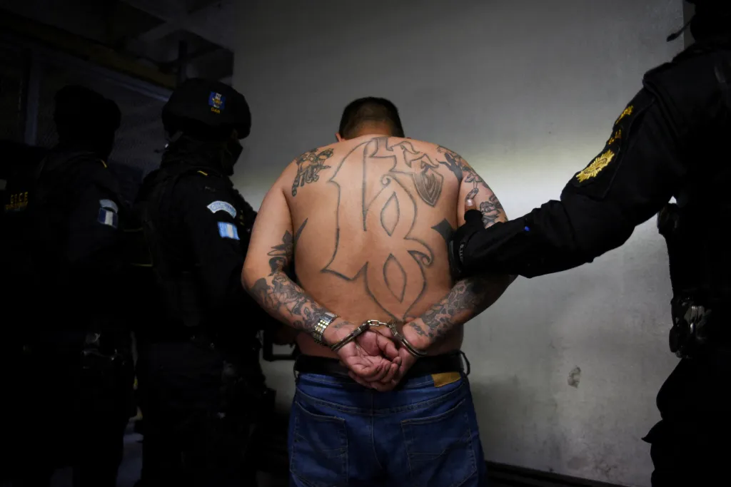 A handcuffed man with numerous tattoos, including a large 