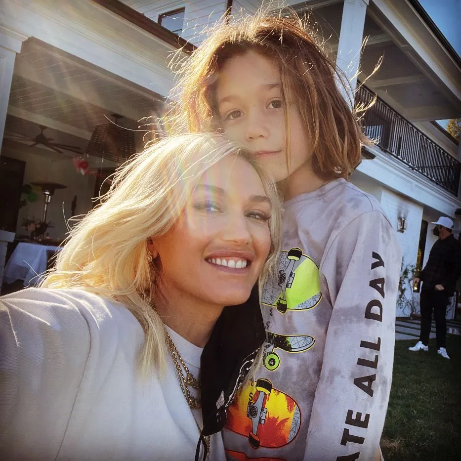 Gwen Stefani smiles next to her son Apollo, who has long brown hair and is wearing a long-sleeved shirt with skateboards on it.