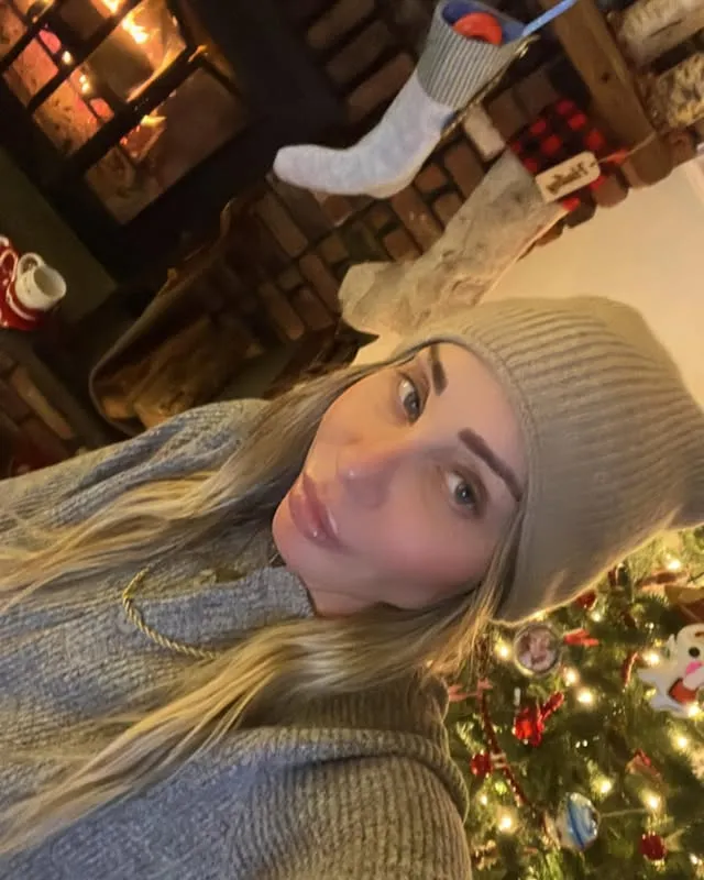 Hailey Glassman poses for a selfie in front of a fireplace and Christmas tree.