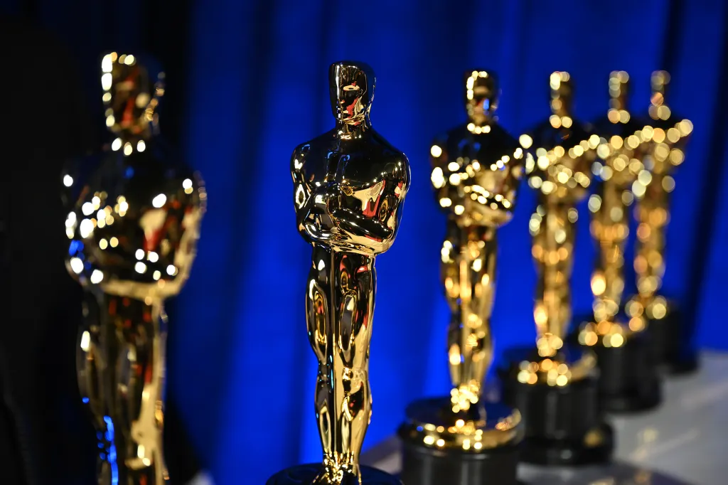 Row of golden Oscar statuettes against a blue background.