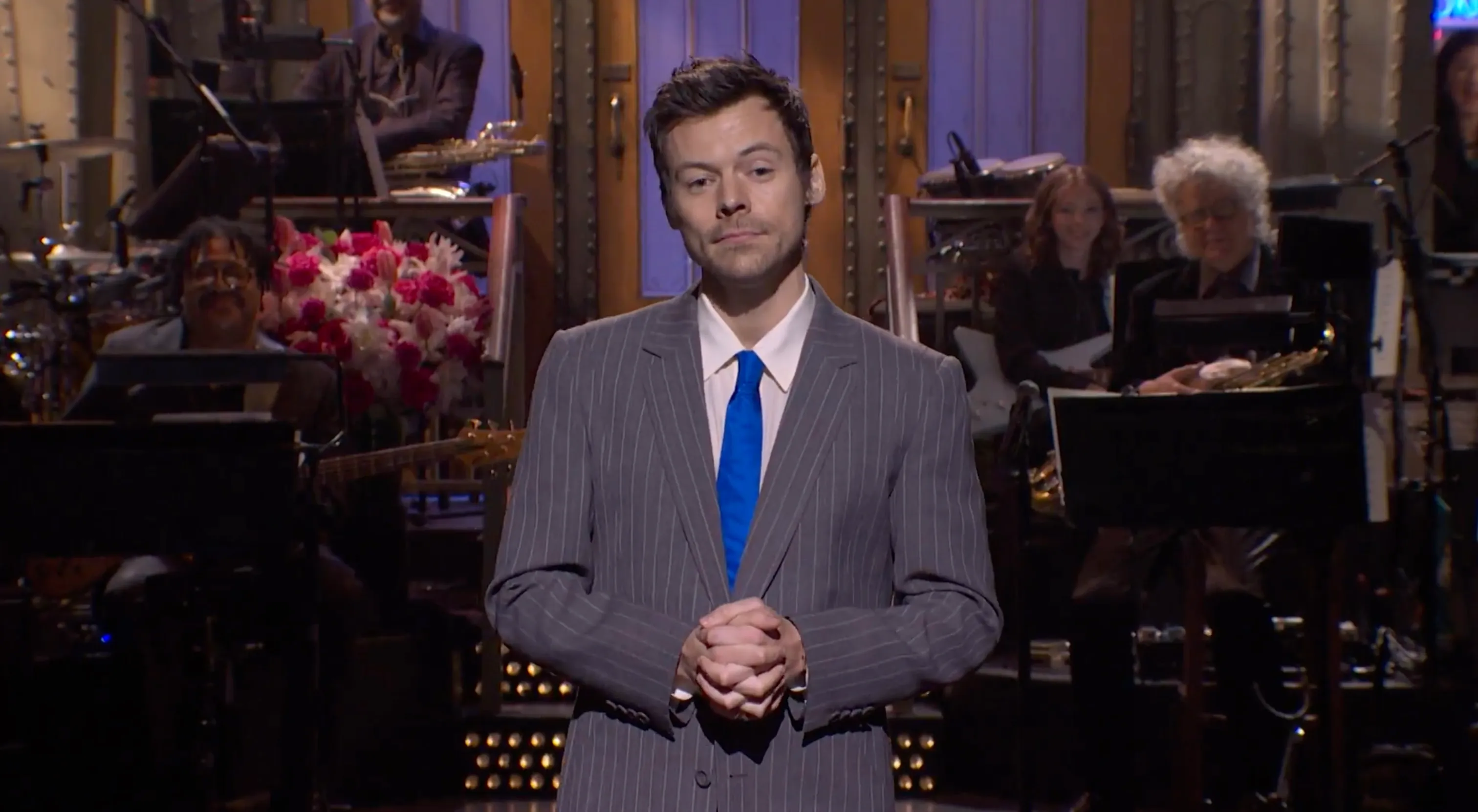 Harry Styles on stage wearing a pinstripe suit and blue tie.