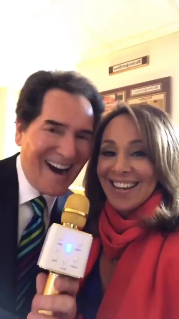Rosanna Scotto and Ernie Anastos smiling while holding a karaoke microphone.