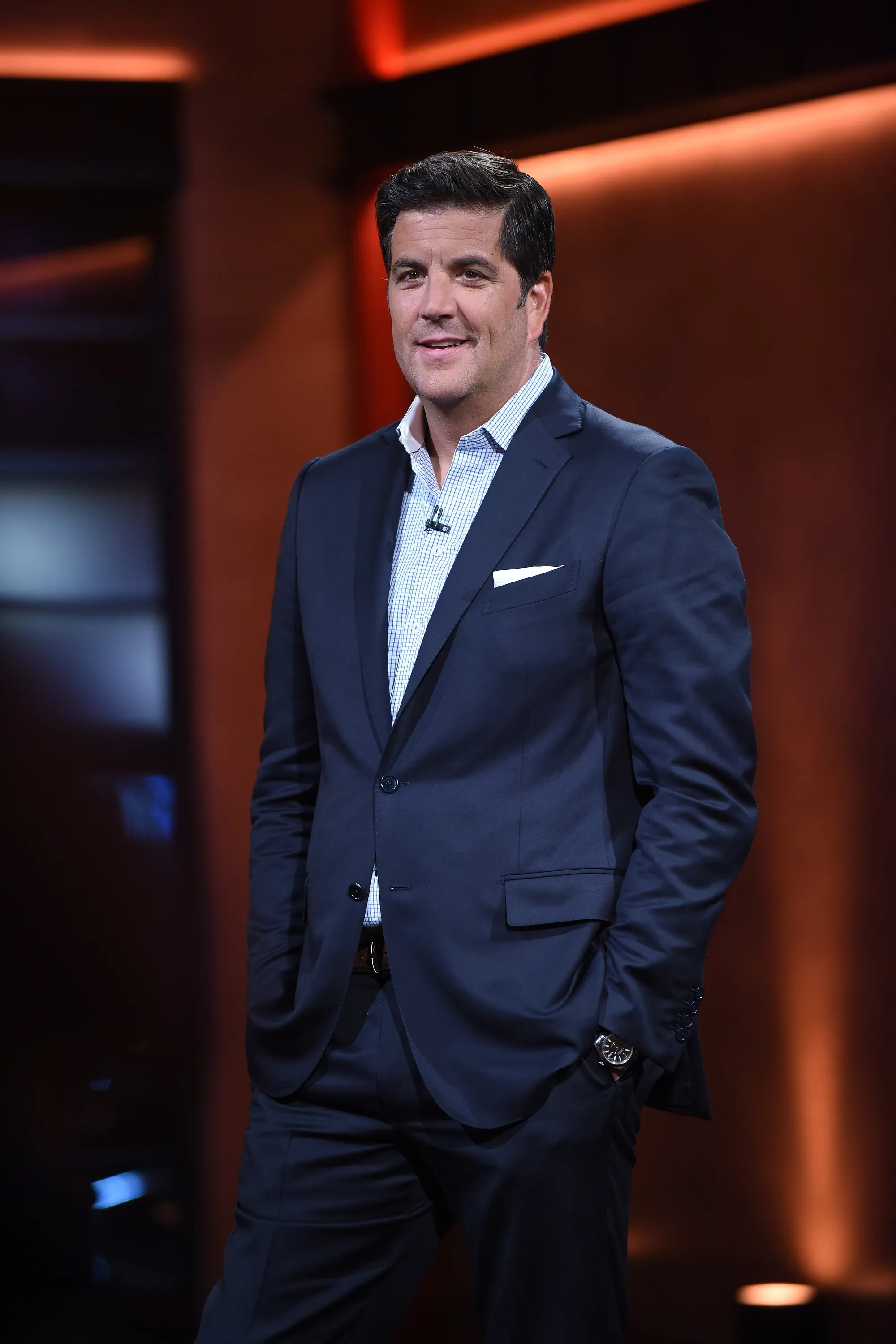 Josh Elliott, host of First Responders Live, poses in a dark blue suit with a checkered shirt.