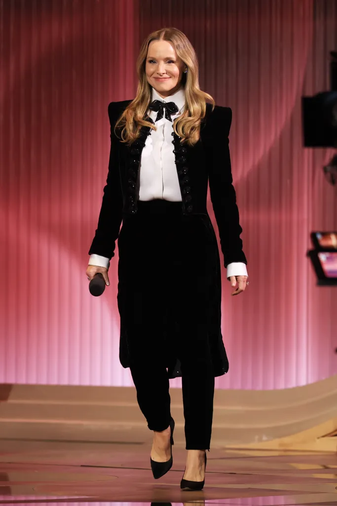 Kristen Bell holding a microphone while speaking onstage at the 32nd Annual Actor Awards.