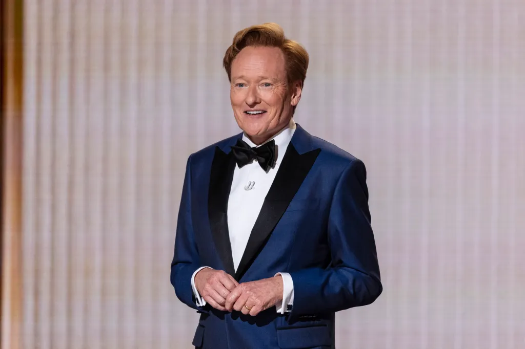 Conan O'Brien smiling while wearing a blue tuxedo with a black bow tie.