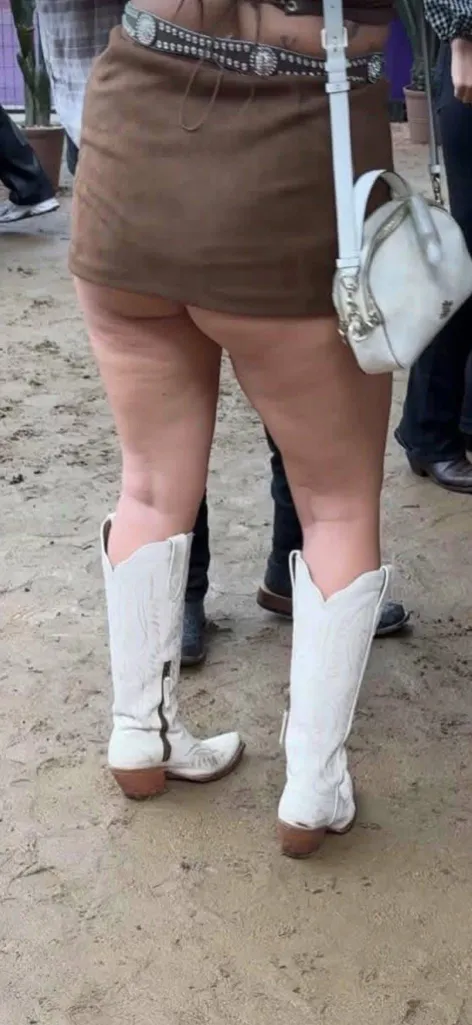 A person from the waist down wearing a brown skirt and white cowboy boots.