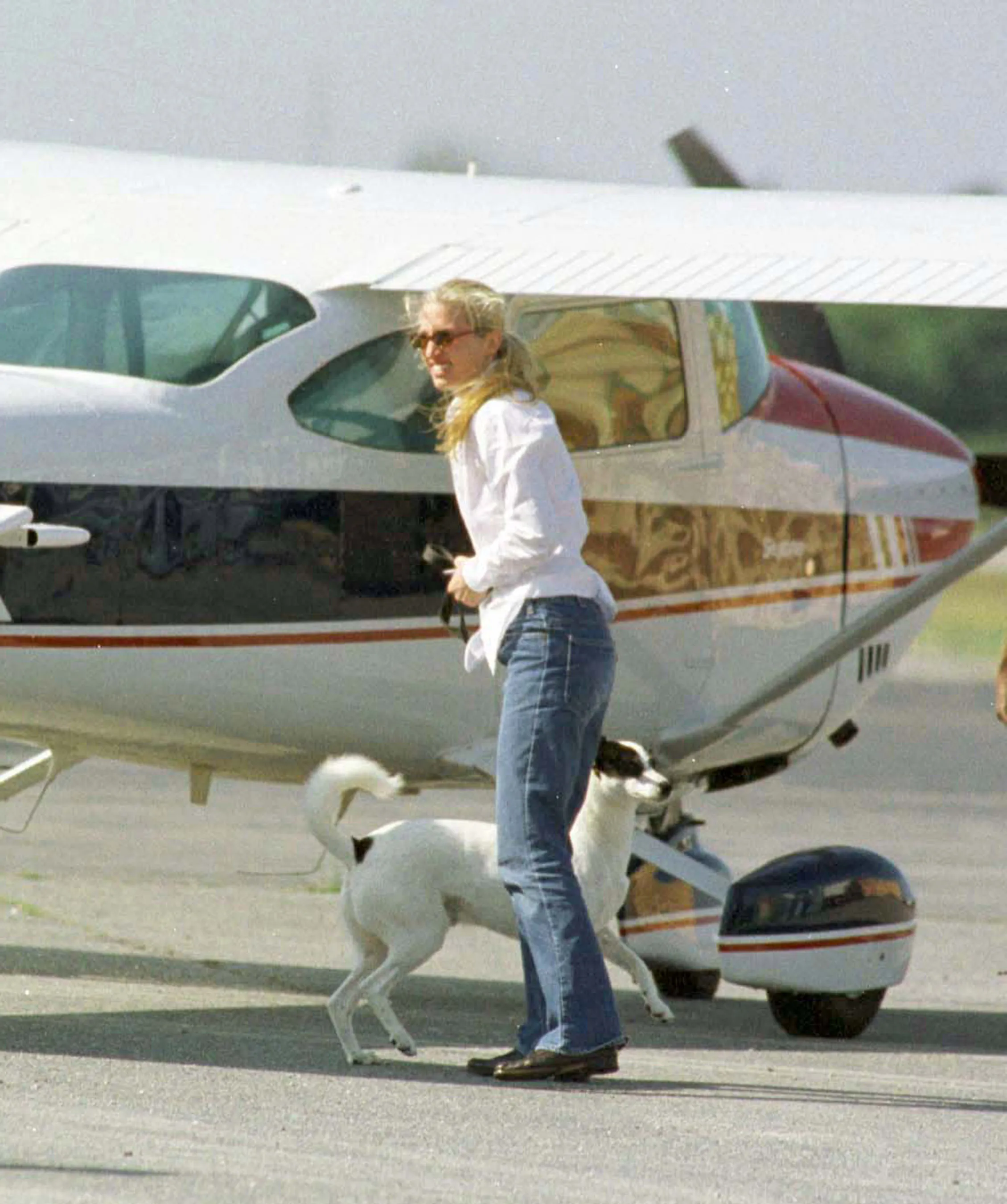Carolyn Bessette with her dog on a leash next to a private jet at Hyannis Airport.