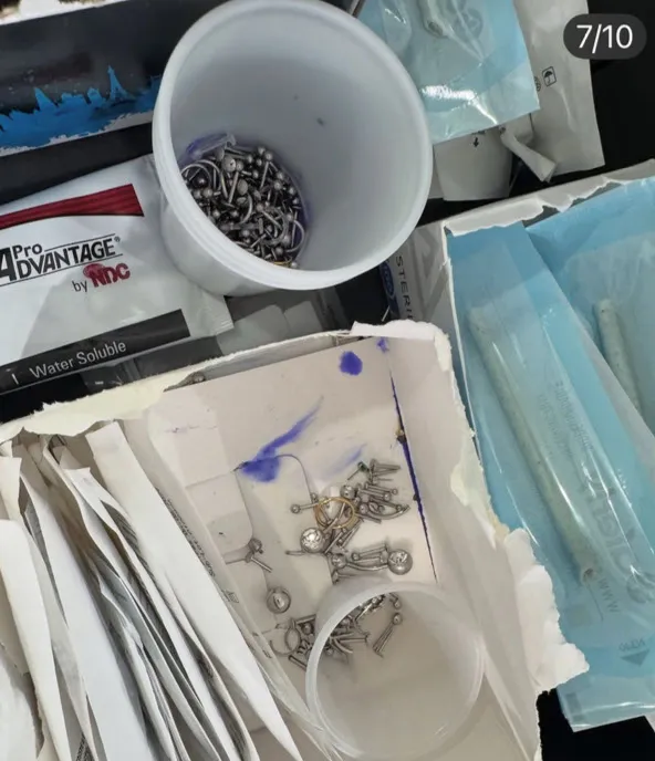 A container of piercing jewelry, some loose, some in clear sterile packaging, suggesting a piercing environment.