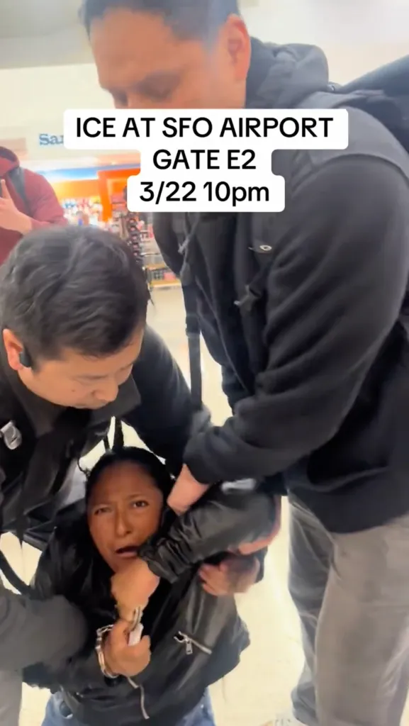 Two ICE officers detain a woman who is handcuffed, as visible text overlay states 
