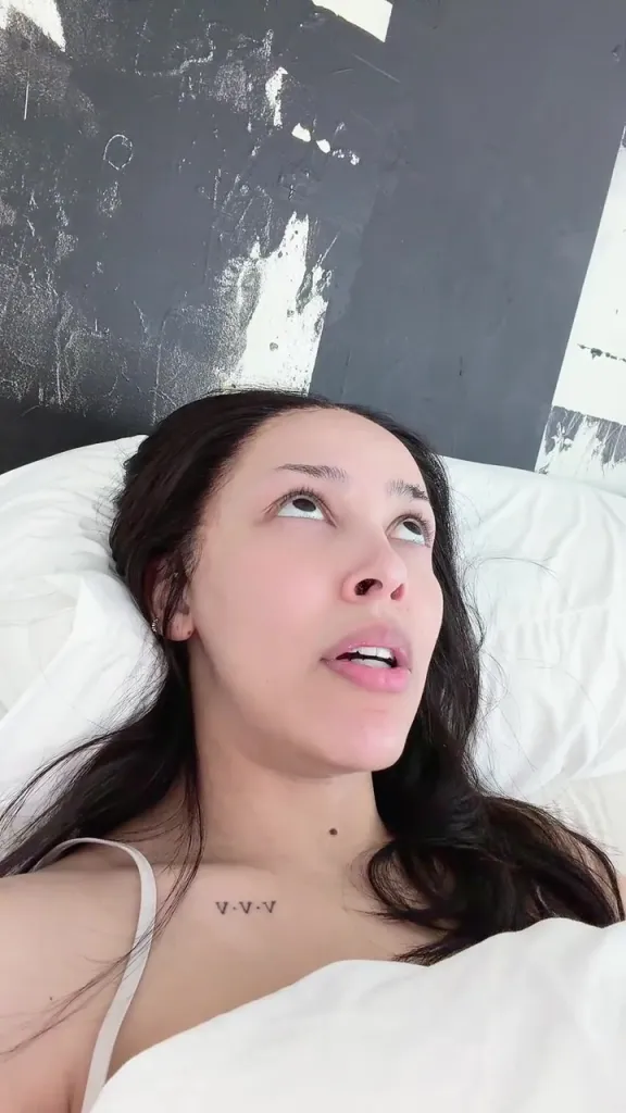 Doja Cat lying in bed, looking upwards with a pensive expression.