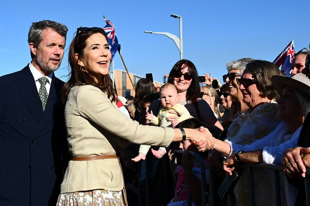 Queen Mary of Denmark shaking hands with a member of the public in Hobart, with King Frederik X beside her and others in the crowd holding an Australian flag.