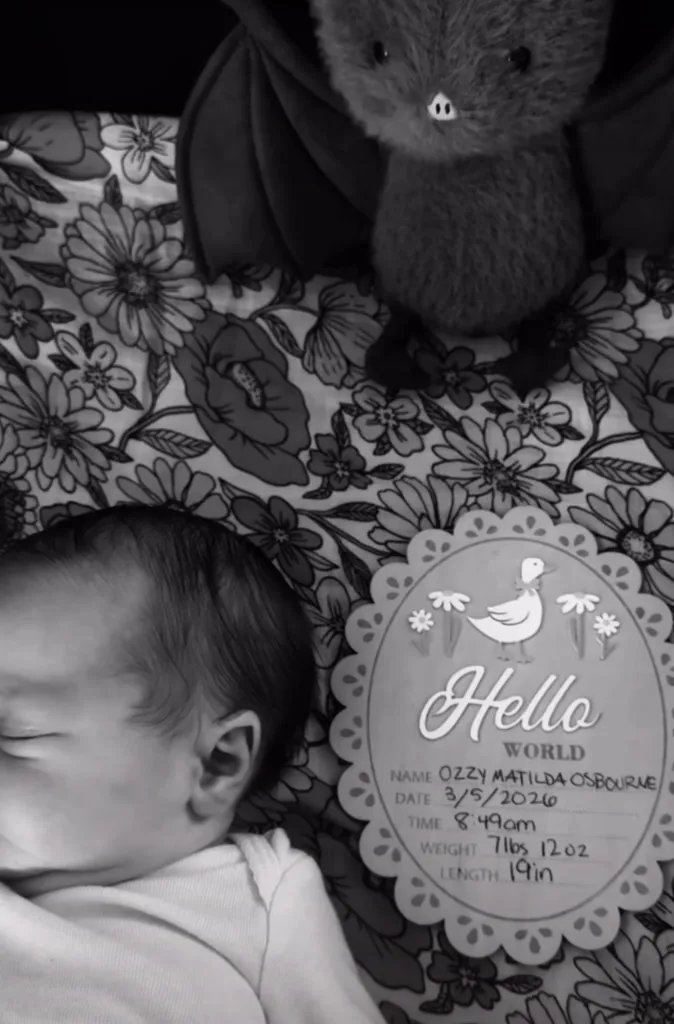 Black and white photo of a newborn baby, a plush bat, and a card that reads 