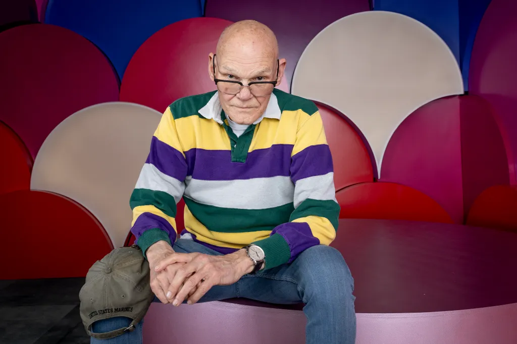 James Carville poses for a portrait wearing a striped polo shirt and glasses, with a 