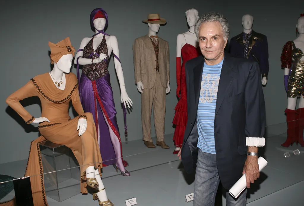 Jean-Pierre Dorleac, designer, standing next to several costumed mannequins in an exhibition.