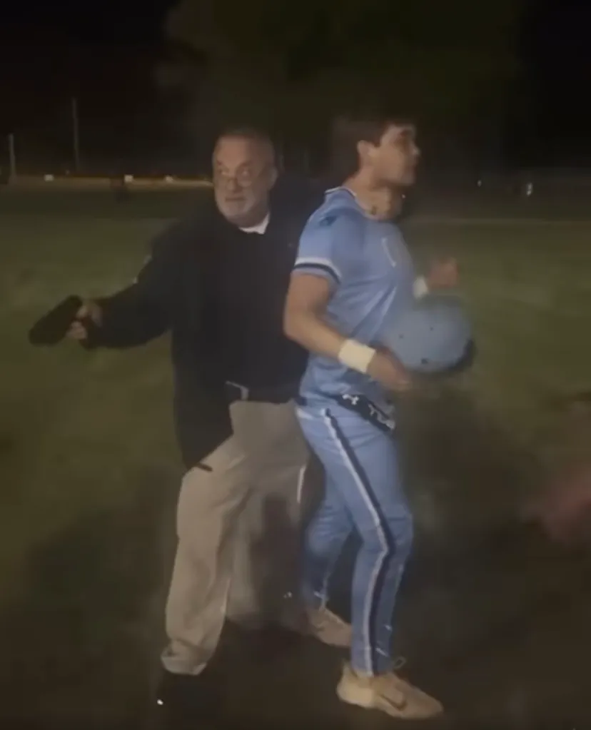 An officer pointing a taser at a young man in a light blue baseball uniform.