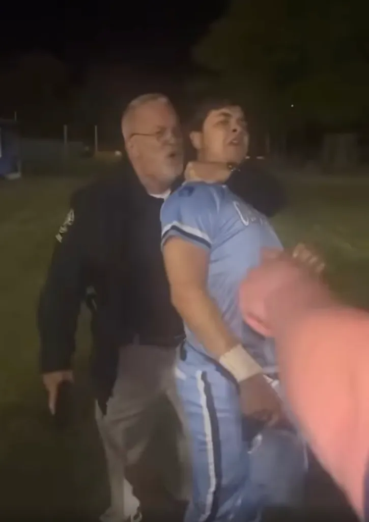 Officer tasing a young man in a baseball uniform.