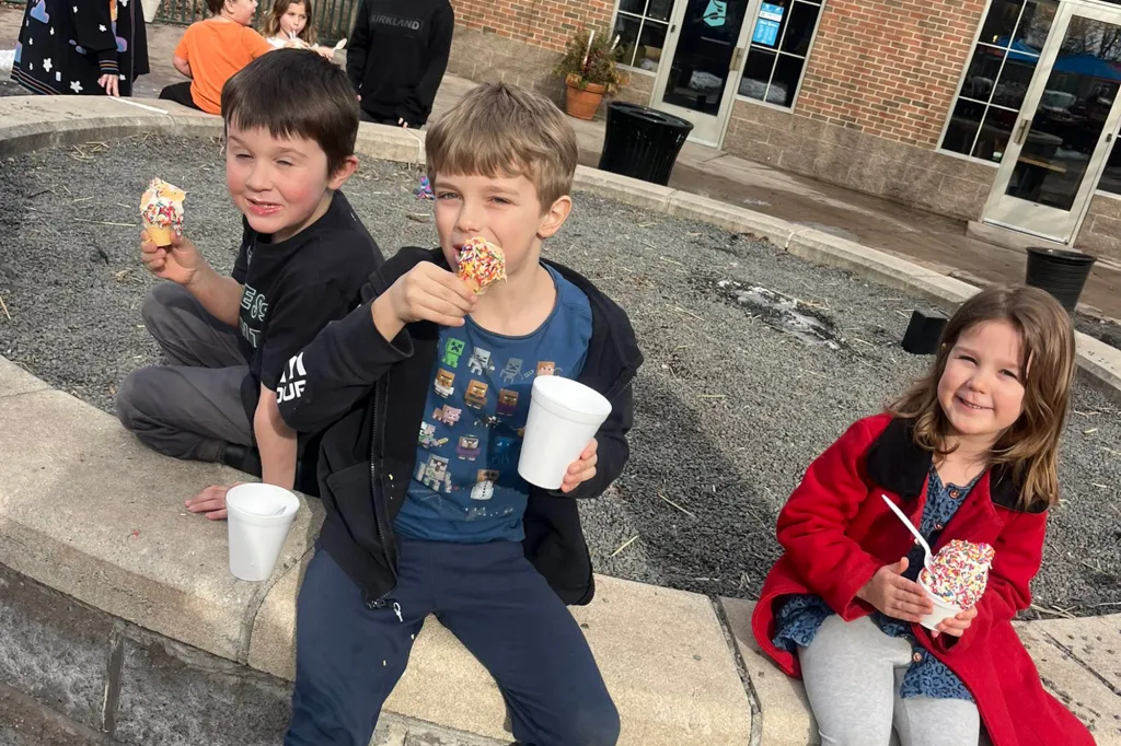 Three children sitting outside eating ice cream.