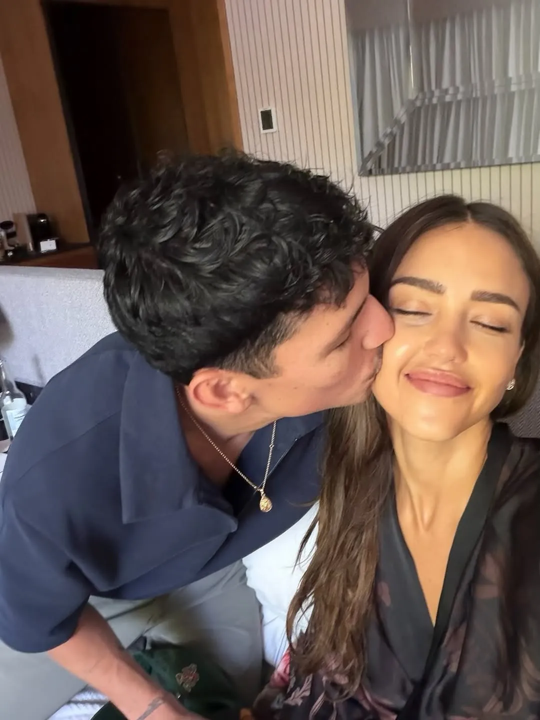 Jessica Alba smiling with her eyes closed as Danny Ramirez kisses her cheek.
