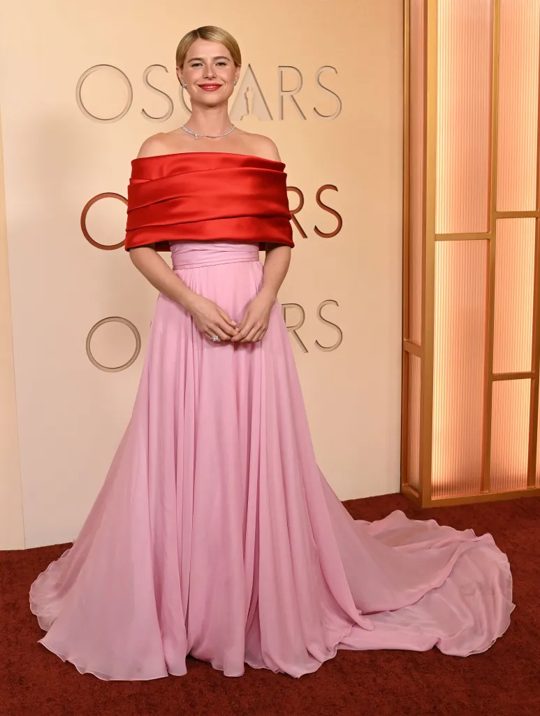 Jessie Buckley in a red off-the-shoulder top and a long pink flowing skirt at the Academy Awards.