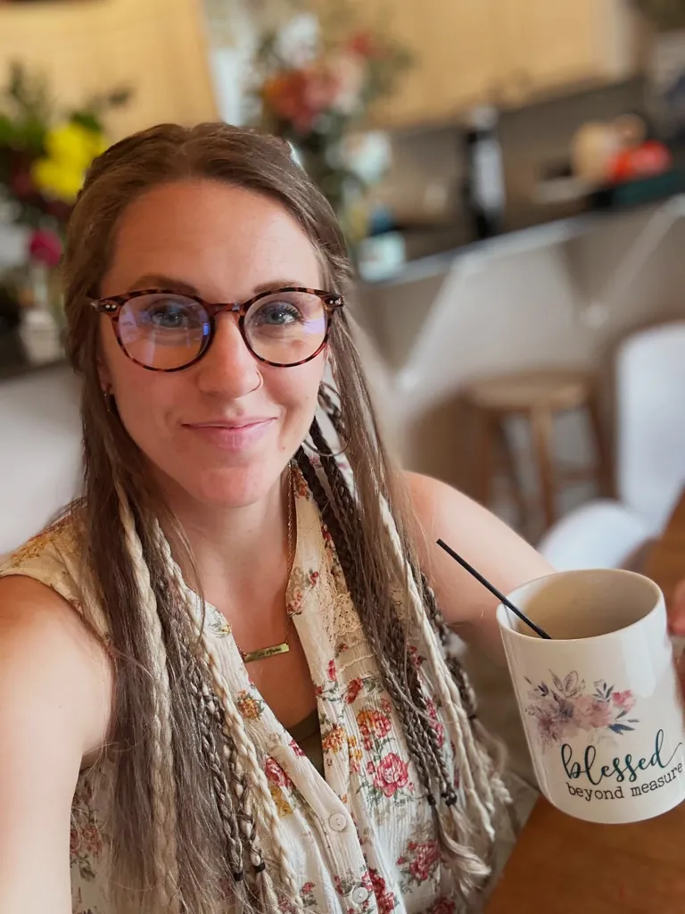 Jill Duggar smiles at the camera, wearing glasses and holding a mug that says 