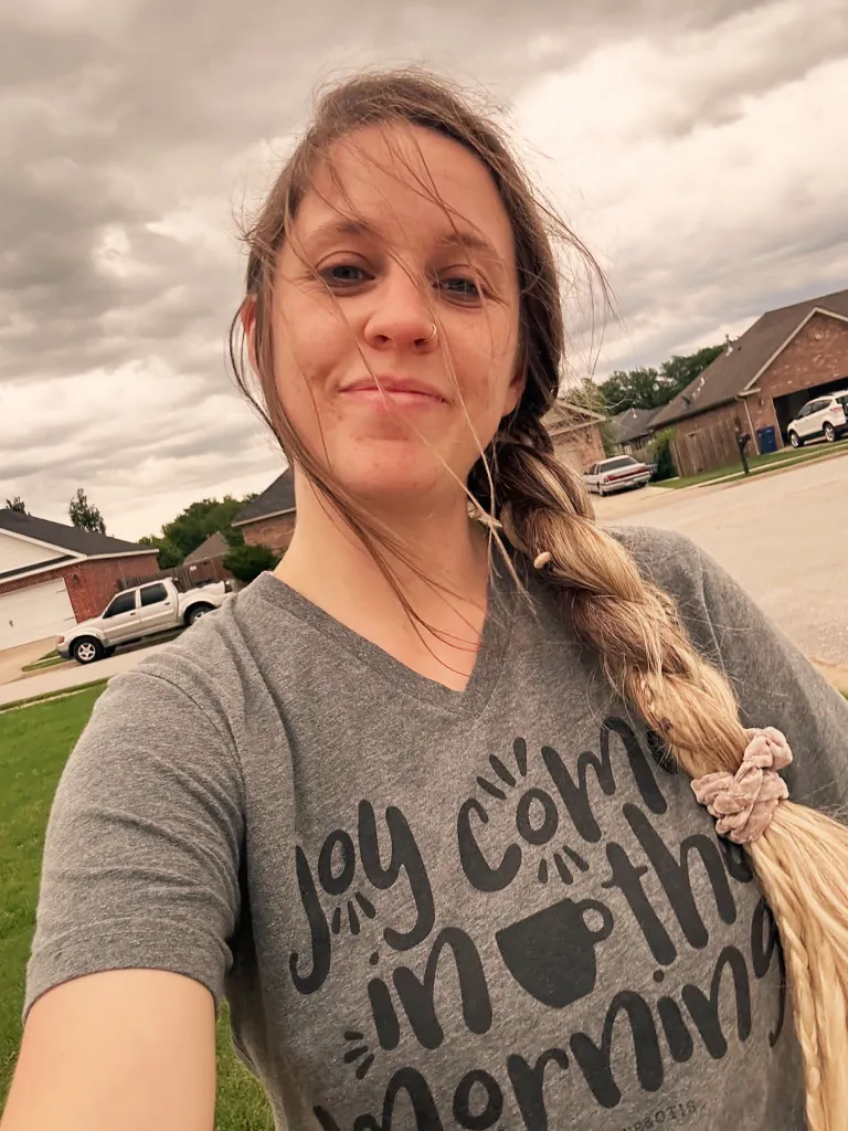 Jill Duggar poses for a selfie, hair blowing in the wind, wearing a grey t-shirt with 