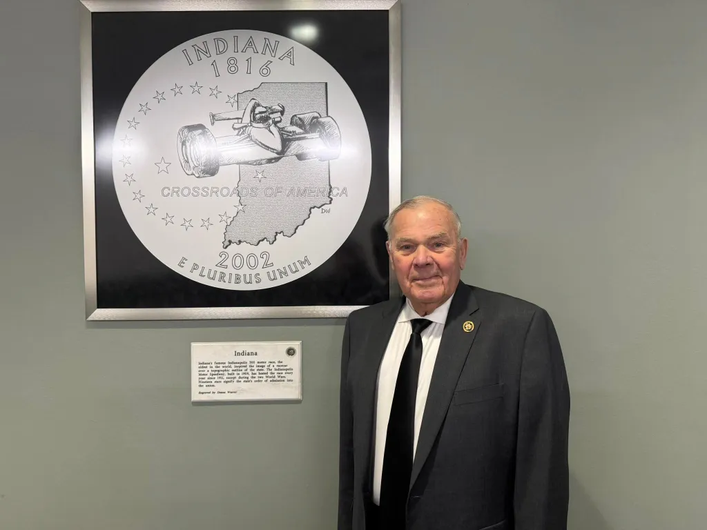 Jim Baird stands next to a large framed image of the Indiana 2002 state quarter.