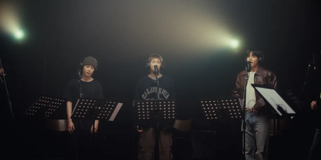 Jimin, RM, and V of BTS singing into microphones in a recording studio.