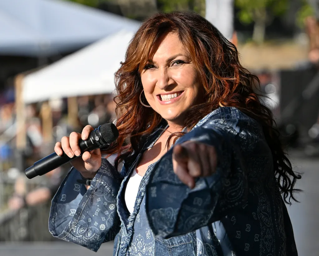 Jo Dee Messina performing on stage, holding a microphone, smiling, and pointing towards the audience.