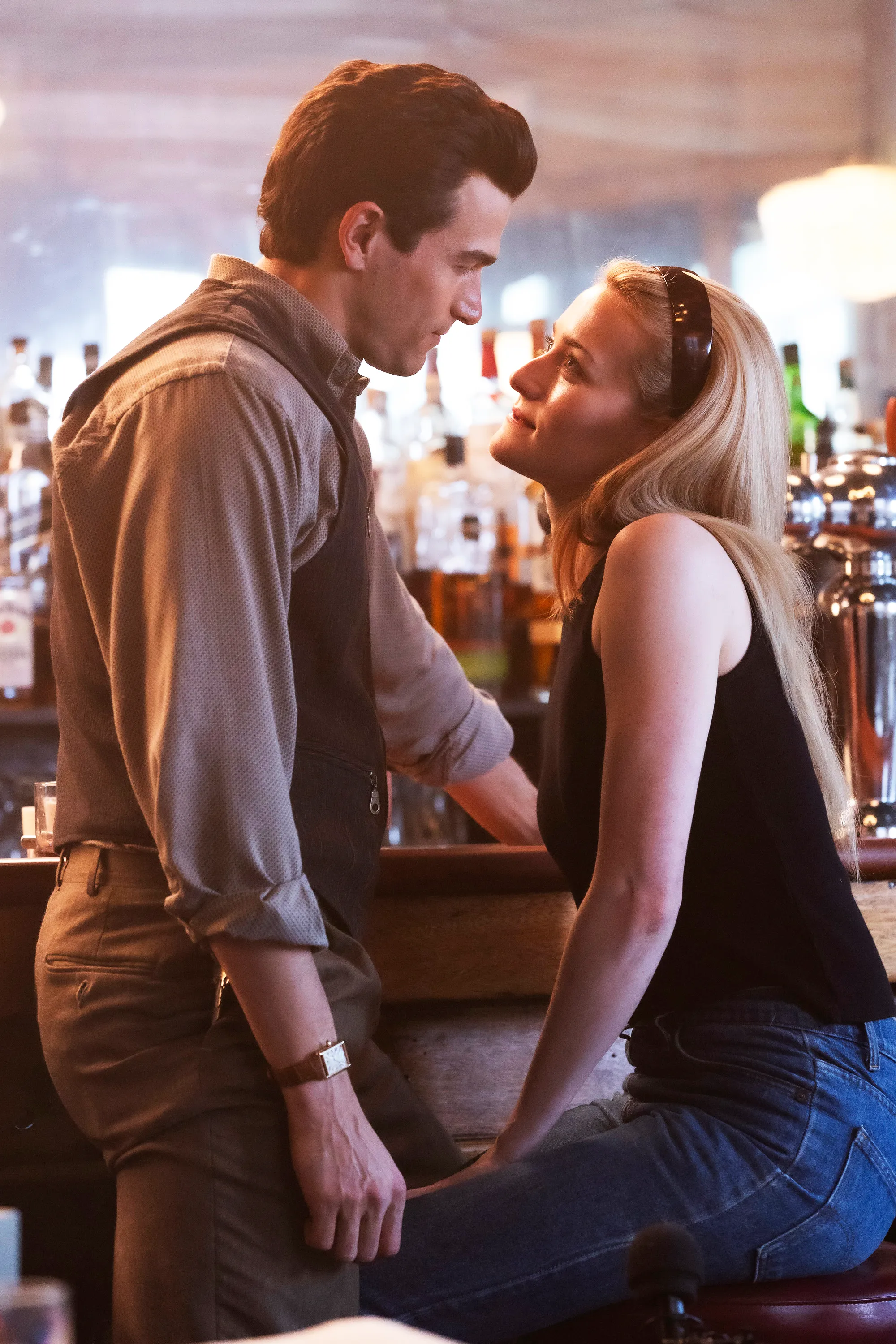 Paul Anthony Kelly as John F. Kennedy Jr. and Sarah Pidgeon as Carolyn Bessette leaning into each other at a bar.