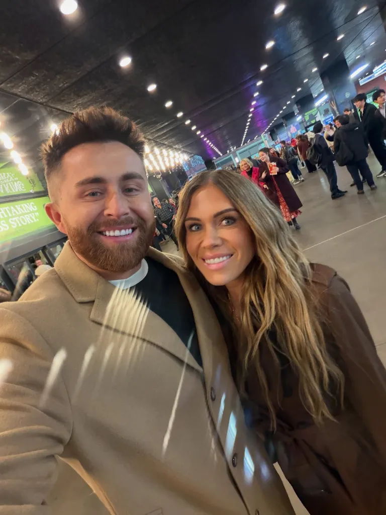 Jordan and Jessi Ngatikaura smiling for a selfie in a busy indoor public space.