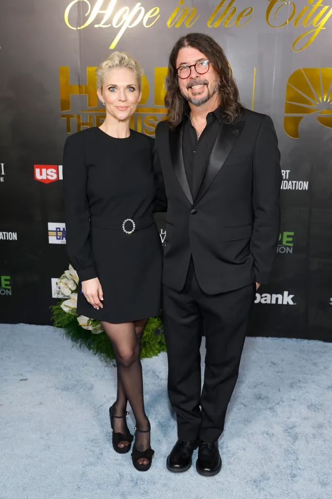 Jordyn Blum in a black dress with a sparkling belt and Dave Grohl in a black suit smiling at a formal event.