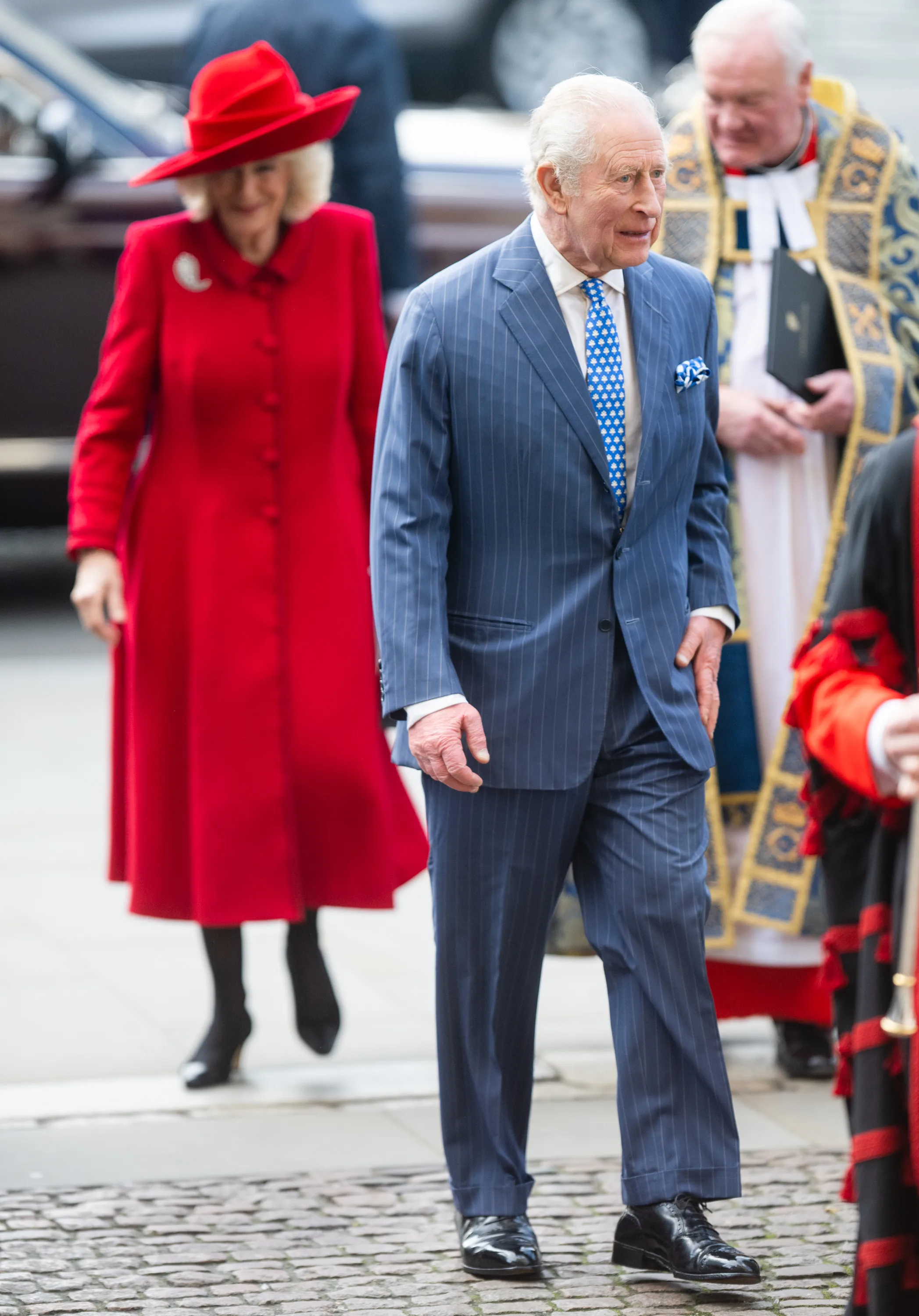 King Charles III in a blue pinstripe suit and Queen Camilla in a red coat and hat attend the Commonwealth Day Service.