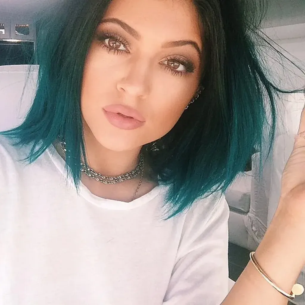 Kylie Jenner with dark hair transitioning to teal at the ends, wearing a white t-shirt and silver necklace.