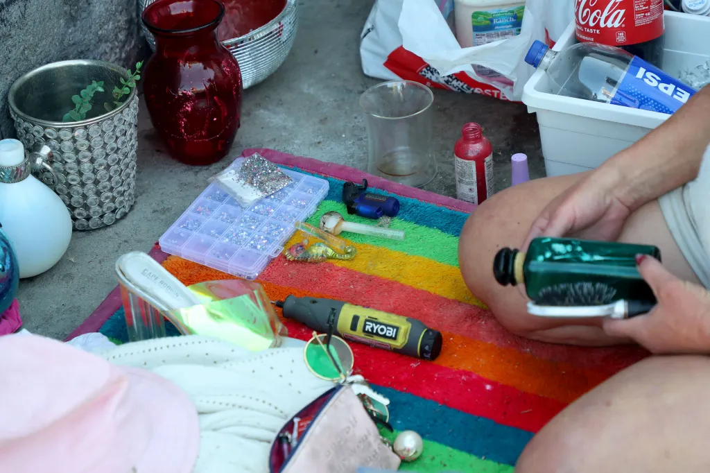 Kween cleaning a glass bottle, surrounded by various personal items on a colorful blanket.
